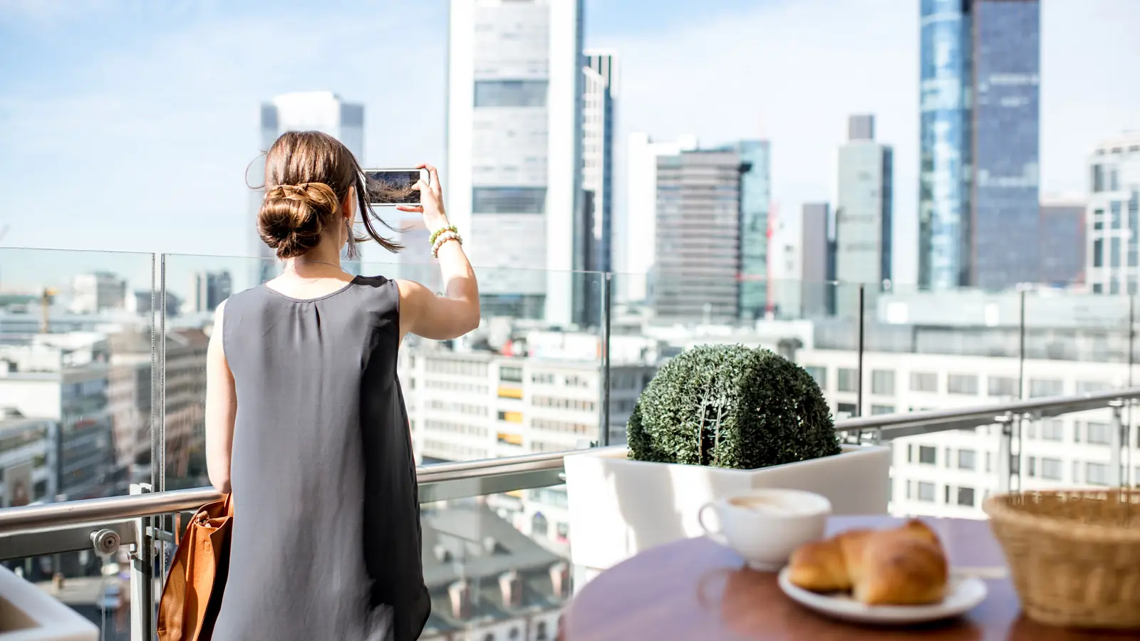 Geschäftsfrau fotografiert die Skyline einer deutschen Großstadt vom Rooftop aus — sinnbildlich für lokale Sichtbarkeit von Mittelstand-Websites in Stuttgart, München, Köln und Hamburg