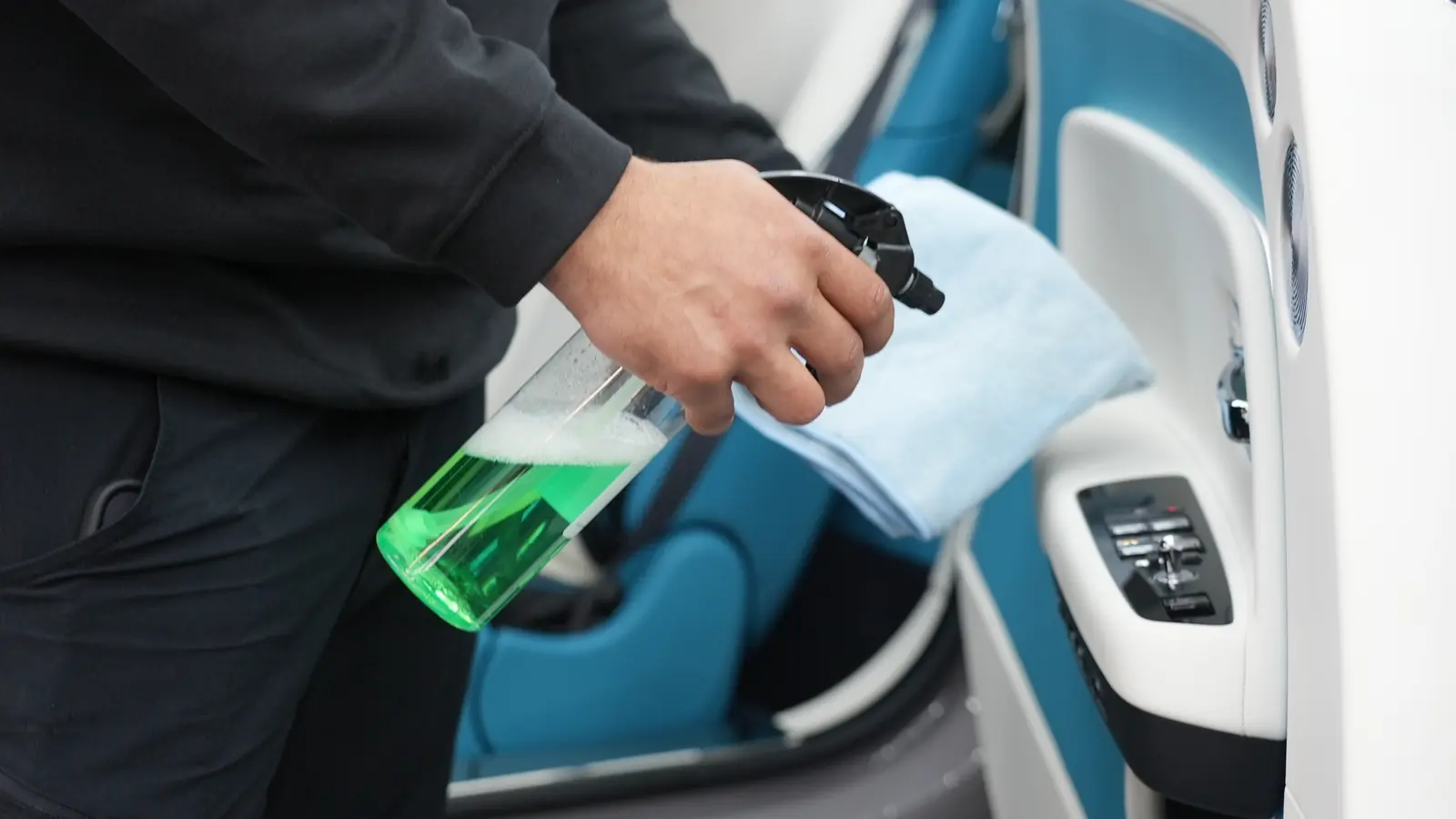 Detailaufnahme der Innenraum-Aufbereitung in einem Premium-Fahrzeug bei Picobello — Hand mit Reinigungsspray und Mikrofasertuch im türkisfarbenen Lederinterieur