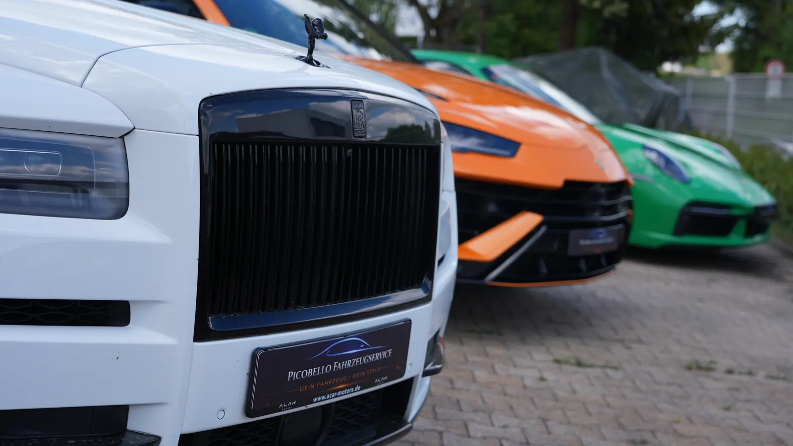 Premium-Fahrzeuge bei Picobello: weißer Rolls-Royce, oranger Lamborghini und grüner Porsche nebeneinander mit Picobello-Kennzeichen im Vordergrund